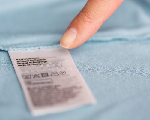 clothes, laundry, people and housekeeping concept - finger pointing to label with users manual on clothing item