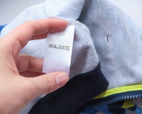 white laundry care clothes label. close up of hand holding label with users manual of clothing item. clothes, laundry, people and housekeeping concept.